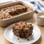 Slice of Delia Smith bread pudding on white plate with cream jug